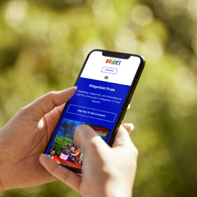 Hand holding cel phone with Pride website on screen