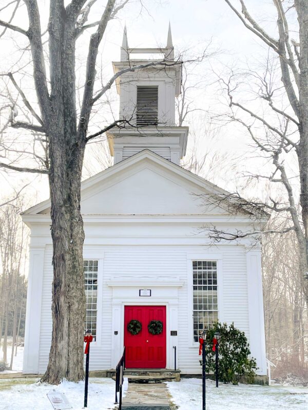 A photo of the meetinghouse.life, a white curch with red welcoming doors on a snowy new england day